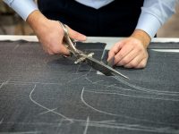 Tailor cutting fabric using large scissors or shears as he follows the chalk markings of the pattern, close up of his hands